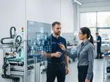 Two manufacturing engineers collaborating in a modern facility, reviewing a product structure tree on a digital screen to align engineering rules.